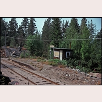 Hagberget hållplats den 31 juli 1975. Hållplatsen är nedlagd sedan 1971, väntkuren är tillbommad och anslagstidtabell saknas, men namnskylten upplyser om var man befinner sig. Foto: Per Niklasson. 
