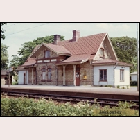 Åskloster station i juli 1969. Stationshuset är mycket litet men har fått ett påkostat utförande värdigt en storstation. De två ljusa sidobyggnaderna är inte ursprungliga utan tillkom troligen på 1920-talet. Bild från Sveriges Järnvägsmuseum. Foto: Okänd. 