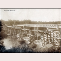 Bro över Norsälven mellan Kil och Fagerås, bilden visar det påbörjade arbetet med den nya bron som skulle stå färdig 1921. Den gamla bron ligger längst bort i bilden och den nya ska byggas på samma plats. En provisorisk bro håller därför på att byggas på en lite lägre nivå. Bild från Järnvägsmuseet. Foto: Okänd. 