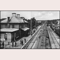 Tranås station före elektrifieringen (1933). Ett norrgående persontåg har gjort uppehåll och några personer rör sig på den smala plattformen till vänster om tåget. Det står ett antal människor på sidoplattfomen vid stationshuset och troligen väntar på ett tåg norrifrån. Bilden är tagen från den gångbro som fanns över bangården. Då gångbron tjänat ut och ersatts med en gångtunnel under spåren, flyttades den till Mjölby där den tjänstgjorde i många år till omkring år 2000. Vykort från förlag Almquist & Cöster. Foto: Okänd. 