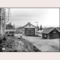 Ramsjö station vid tiden för öppnandet 1881 med ett stort stationshus och ett litet godsmagasin. I bakgrunden ses ett vattentorn av trä, som senare ersattes av ett större i tegel. Bild från Sveriges Järnvägsmuseum. Foto: Okänd. 
