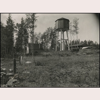 Stavsjö station hade ett vattentorn av en mindre vanlig typ. Det är rivet sedan länge, troligen skedde det under 1980-talet. I bakgrunden syns skjulet för omlastning mellan Stavsjö järnväg och SJ. Bilden - från Sveriges Järnvägsmuseum - är tagen mellan 1915 och 1932. Foto: Okänd. 