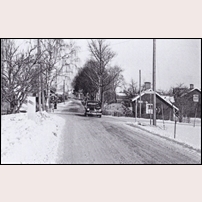 Tororp banvaktsstuga under senare delen av 1950-talet. Järnvägsövergången ligger bortom stugan (se kryssmärket och fällbommen). Vägvisaren visar gamla vägen mot Linköping. Bilen, troligen en Fiat 1400, kommer på vägen från Klockrike kyrka.   Foto: Okänd. 