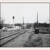 600 Spång låg till höger om järnvägen strax bakom ryggen på fotografen. När bilden togs 1957 var den dock redan riven. Det var grindarna vid den här vägkorsningen som banvakten eller hans familjemedlemmar hade i uppgift att bevaka. Långt borta i kurvan syns en ljus fyrkant till höger om spåret, det är väntkuren vid Östra Spångs hållplats. Vägen till vänster är "riksettan". Den finns fortfarande kvar som länsväg, medan väg E 4 övertagit den långväga trafiken och fått motorvägsstandard med en ny sträckning öster om Örkelljunga. Fotoriktning österut. Bild från Järnvägsmuseet. Foto: Okänd. 