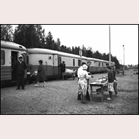 Hackås station den 24 juli 1964 med den närmast legendariska "Beda i Hackås" som servar resenärerna i tåg 872 (för visst är det väl hon själv på bilden?). Beda (1914-1983) drev rörelsen i många år, trots att SJ på senare år försökte motarbeta henne genom att förbjuda konduktörerna att ta upp beställningar. Efter att hon slutat upprätthölls verksamheten några år av en anhörig och därefter en kortare tid av en utomstående person. Foto: Jan-Anders Wihren. 
