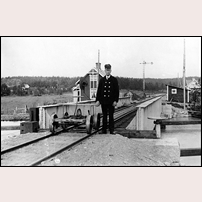 Banvakten Arvid Johansson poserar med sin dressin invid bron över Göta kanal. Bilden är tagen tidigast 1918 (Johansson började sin tjänst här i november 1917). Vissa tider bör tillsynen och manövreringen av bron ha varit hans huvuduppgift. Han skrevs till och med in i församlingsboken såsom brovakt. Bron är en asymmetrisk svängbro, dvs den är lagrad så att ena broarmen är längre än den andra. Bakom banvakten syns hans bostad, banvaktsstugan i Lyrestad, och till höger skymtar stationshuset.
 Foto: Erik Rud. 