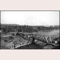 Bron över Göta älv väster om Vargön 1945. Närmast ses den utsprängda Huvudnäskanalen, därefter Göta älvs huvudfåra där den ursprungliga stålbron ligger kvar med sina hängande bågar. Längst bort ligger en ny bro som byggts på land redo att ersätta den gamla. Foto: Okänd. 
