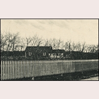 Ronehamn station omkring 1910. Delförstoring av ett okänt vykort som i stort sett visar ett staket och ett en byggnad i bakgrunden. Järnvägen bör gå på bortsidan av huset och Ronehamns hamn ligger åt höger och Hemse åt vänster. Det verkar vara den enda bild av stationen som finns att tillgå. Foto: Okänd. 