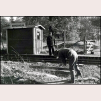 Borgsholm hållplats omkring 1960. Den ene banarbetaren håller på att greja något med stängseltråden medan den andra övervakar arbetet. Bilden tillhandahållen av fotografens son Willy Forsström. Foto: Clarence Forsström. 