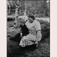 Banvaktshustrun Emmy Gustafsson troligen på 1930-talet. Hon förestod hållplatsen och poststationen 1925 - 1938. Hunden heter Tjappa och ser ut att vara en lapphund. Bild från Järnvägsmuseet. Foto: Okänd. 