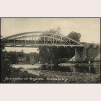 Bro över Hedströmmen väster om Skinnskattebergs station omkring 1908. Bilden är tagen i sydlig riktning och i bakgrunden syns Skinnskattebergs herrgård som med tiden kom att inhysa Skogsmästarskolan. Landsvägsbron på andra sidan järnvägsbron är ännu inte byggd. Bild från Järnvägsmuseet. Foto: Okänd. 