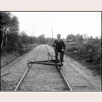 Banvakten Janne Johannesson vid Skogsgärde station okänt år. Banvallen är ogräsfri och ritsen dragen. Med all sannolikhet är bilden tagen invid banvaktsstugan, som ligger till höger utanför bilden. Notera att dressinen som Johannesson sitter på inte bara är likadan som hans företrädares, det är samma fordon! Bild från Drängsereds Hembygdsförening. Foto: Okänd. 