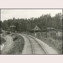 Ekolsund station, infarten från öster före 1947 (året som linjen elektrifierades). Stugan med den ljusa skorstenen är banvaktsstugan 122 Ekolsund, vid SJ nummer 768. Efter svängbron ligger det stora vattentornet och längst till vänster ett litet godsmagasin. Notera också de många trådarna för telekommunikation. Bild från Järnvägsmuseet. Foto: Okänd. 